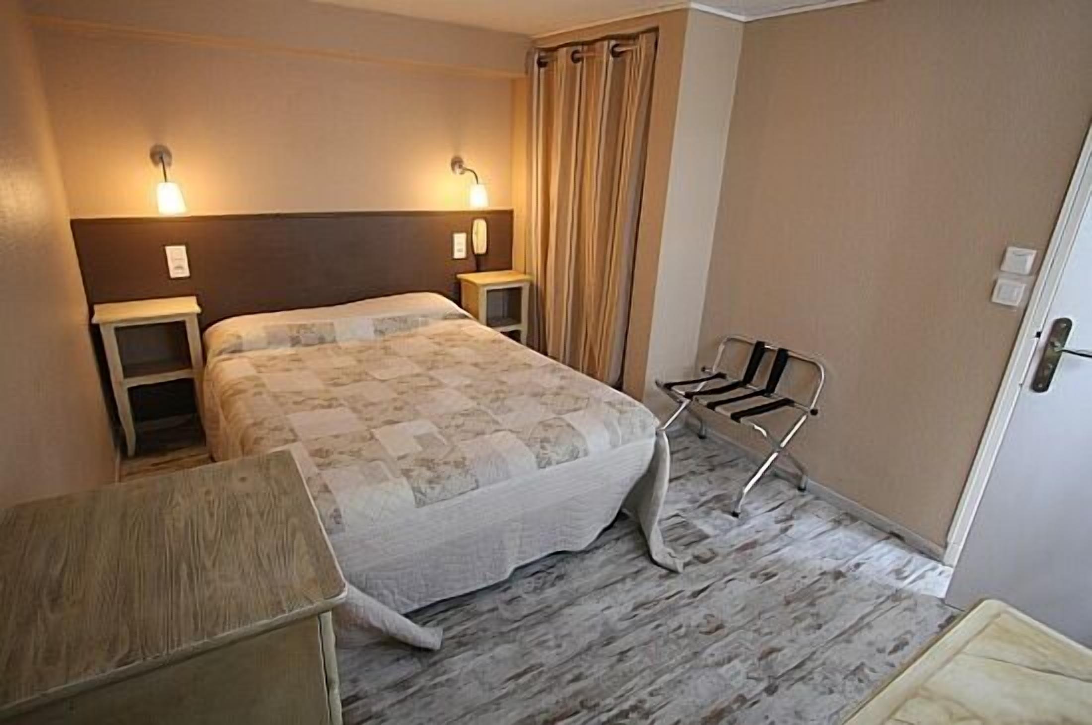 A hotel room with a bed, bedside tables, a chair, and a curtain.