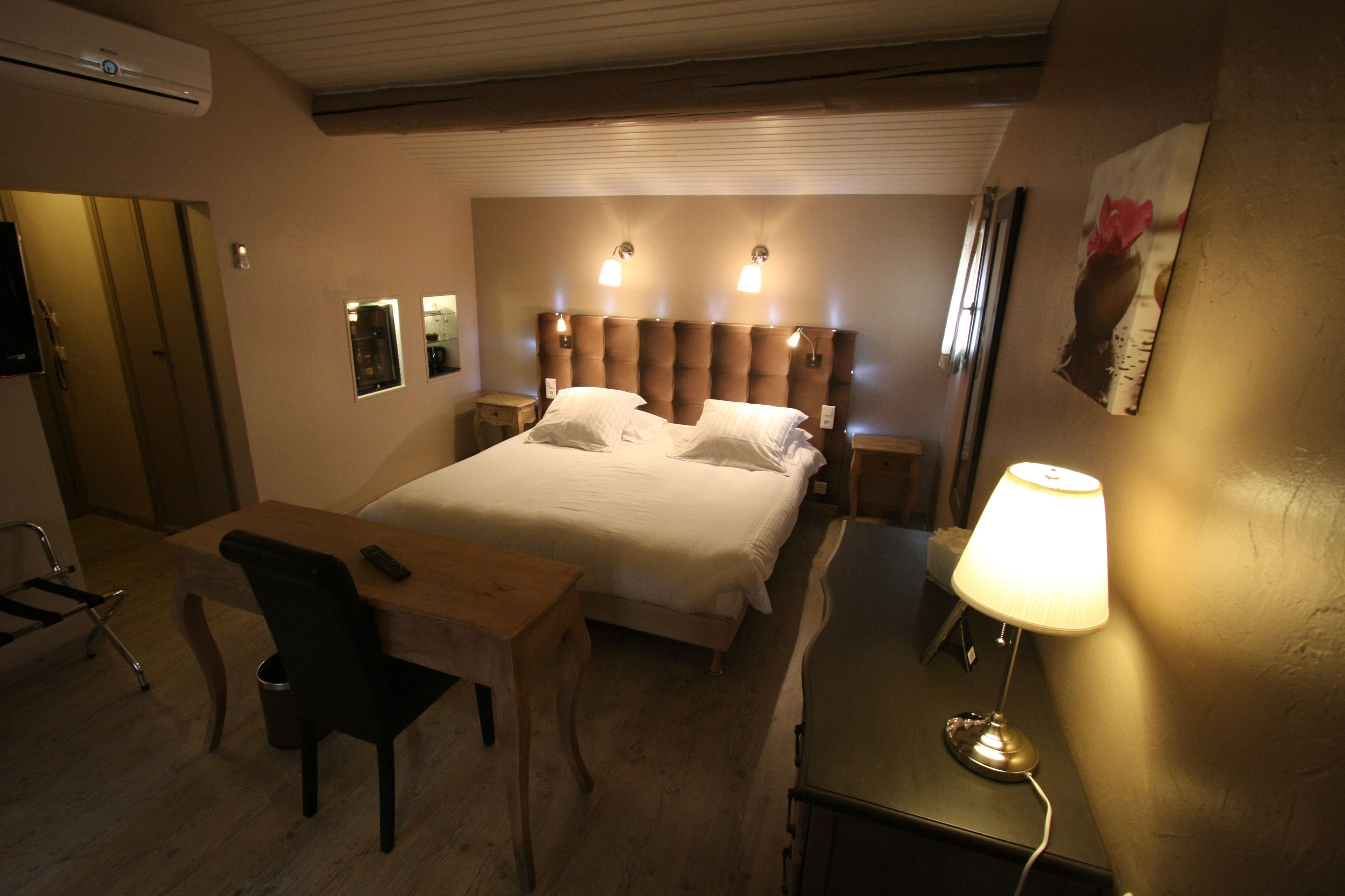 A hotel room with a bed, a desk, a chair, a lamp, and a wall-mounted picture.