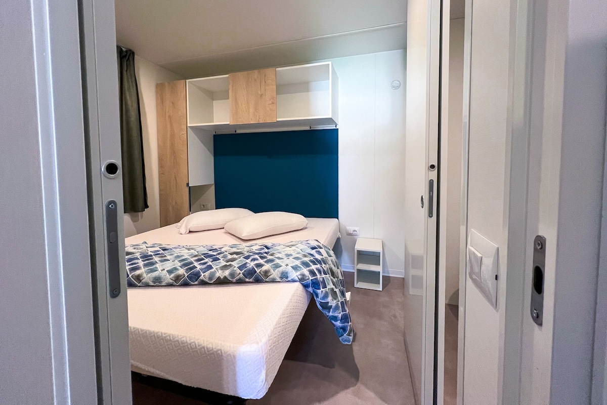 A compact bedroom with a bed, a headboard, a wardrobe, and a small bedside table.