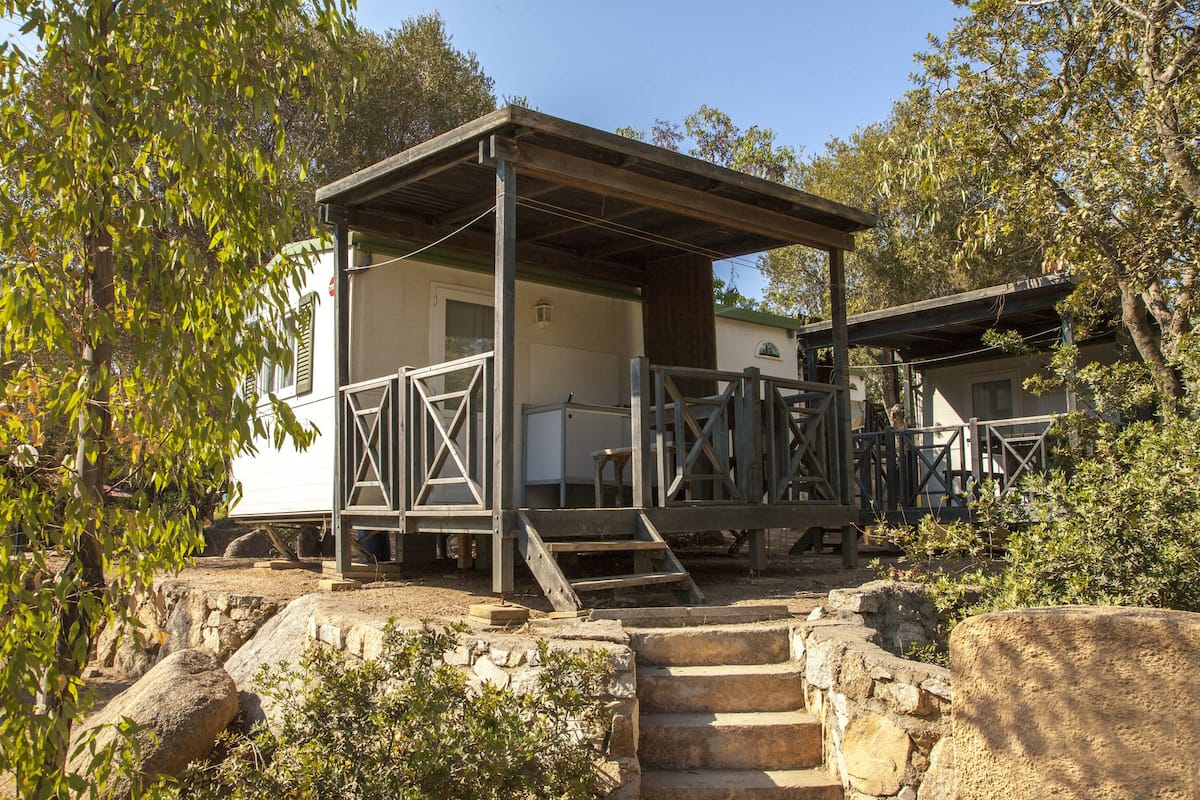 Un chalet rustique doté d’une terrasse en bois et d’un escalier en pierre, entouré d’arbres.