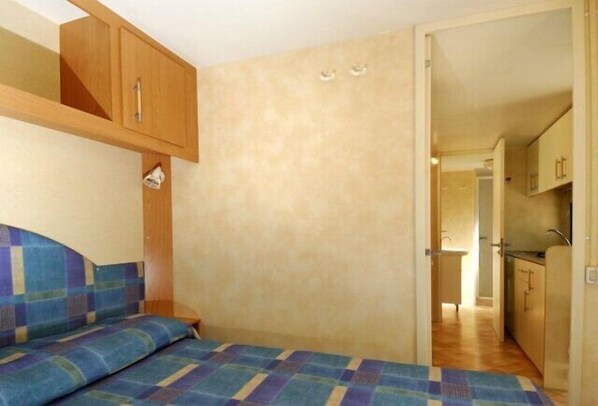 A compact room with a bed, a small table, and a kitchenette area. - Camping Village Capo D'Orso (Palau)