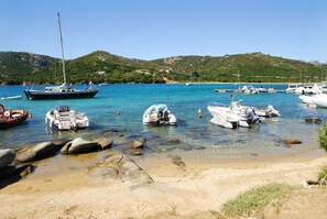 A marina with various boats docked, clear water, and a hilly landscape in the background. - Camping Village Capo D'Orso (Palau)