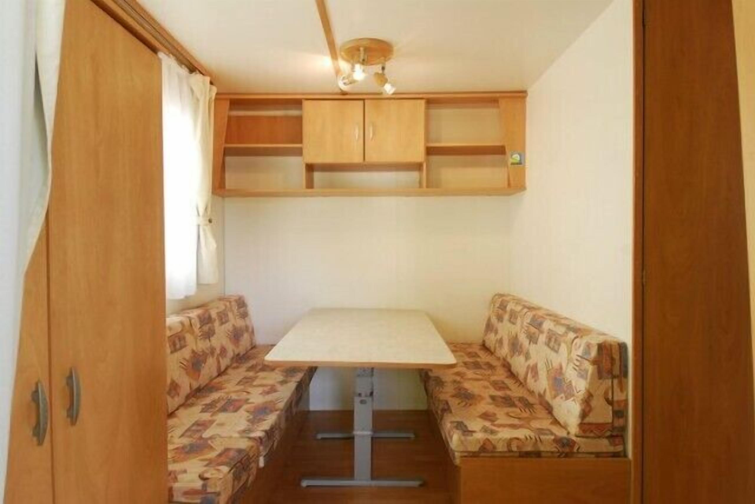 Ein kompaktes Wohnmobil-Interieur mit einem zentralen Tisch, zwei gepolsterten Sitzbereichen und Hängeschränken.
