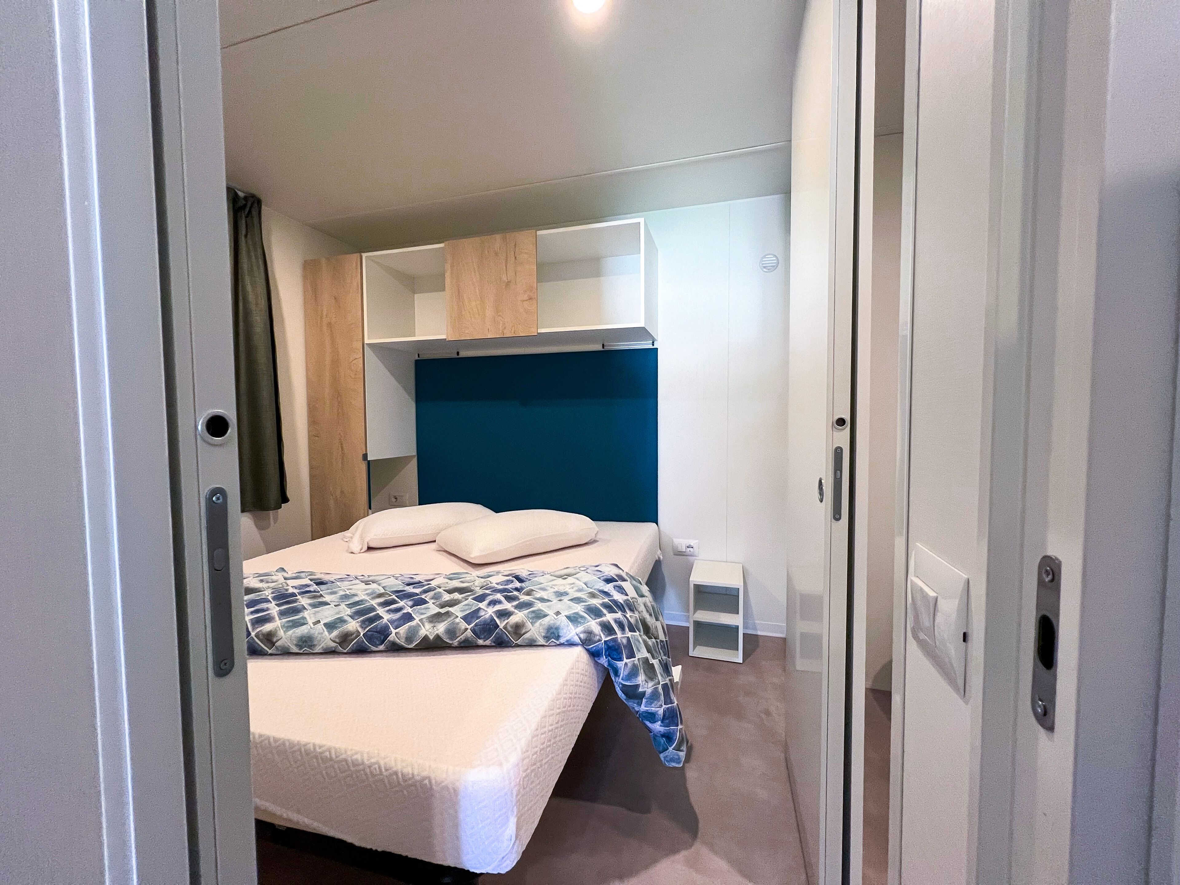 A compact bedroom with a bed, a headboard, a wardrobe, and a small bedside table.