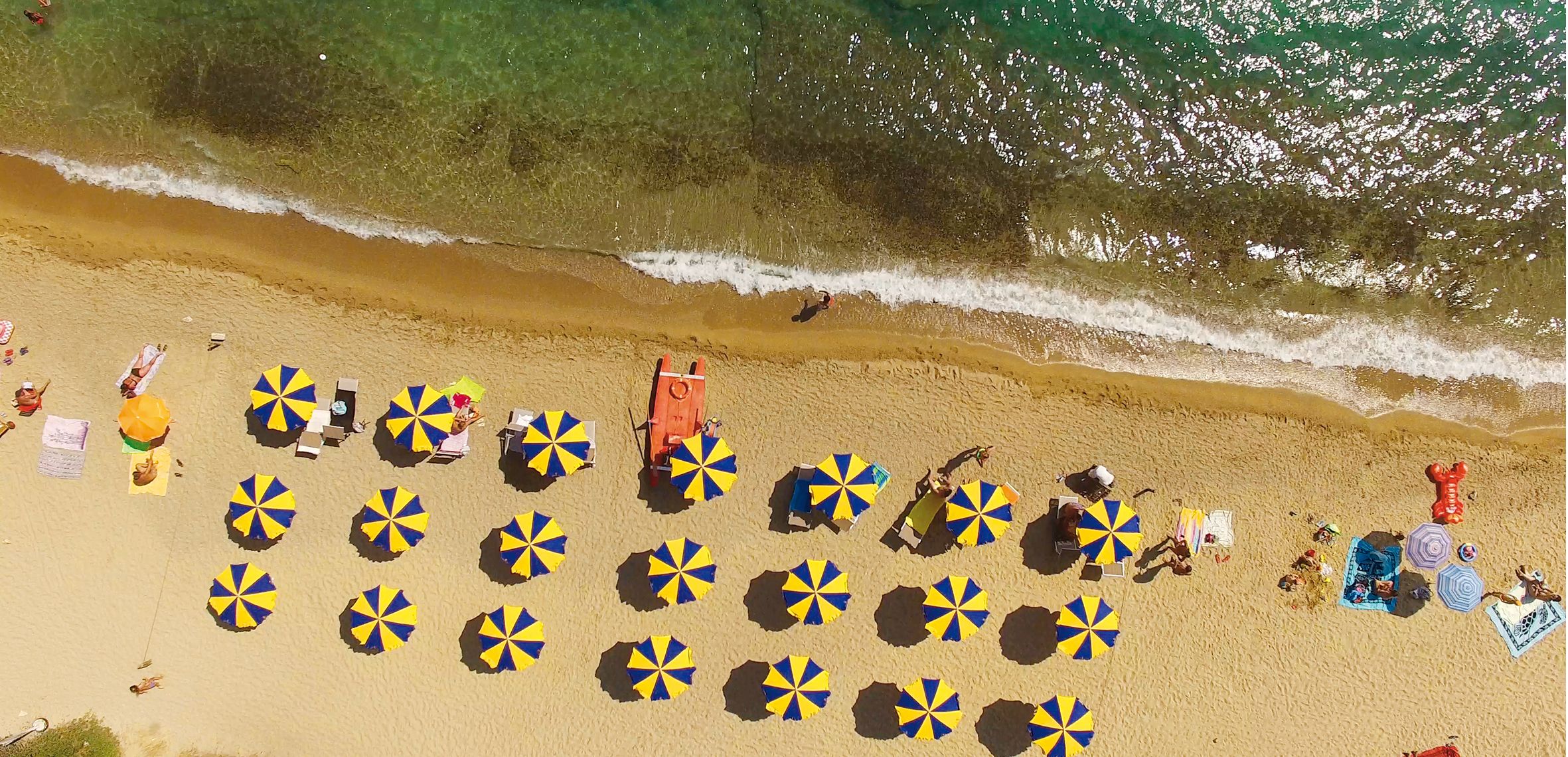 An aerial view of a beach with numerous sun umbrellas and beach chairs arranged in rows.
