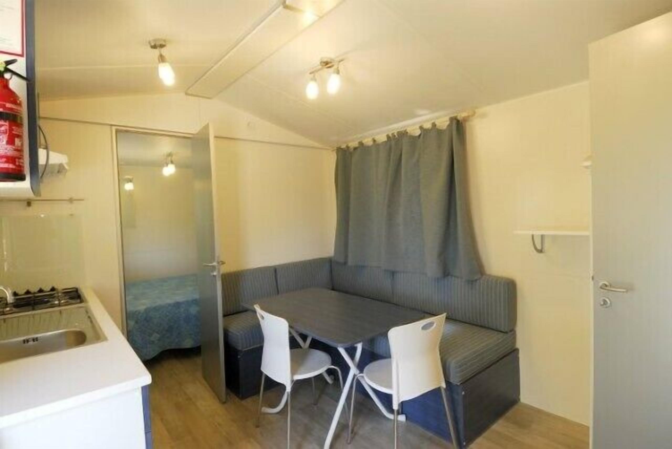 Une petite cuisine équipée avec un évier et une cuisinière, une petite table à manger avec deux chaises et un banc agrémenté d’un rideau.