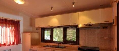 A compact kitchen with a dining area, a window with curtains, and a red sofa.