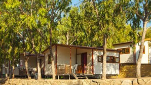 A row of single-story houses with a porch, surrounded by trees. - Camping Village Capo D'Orso (Palau)