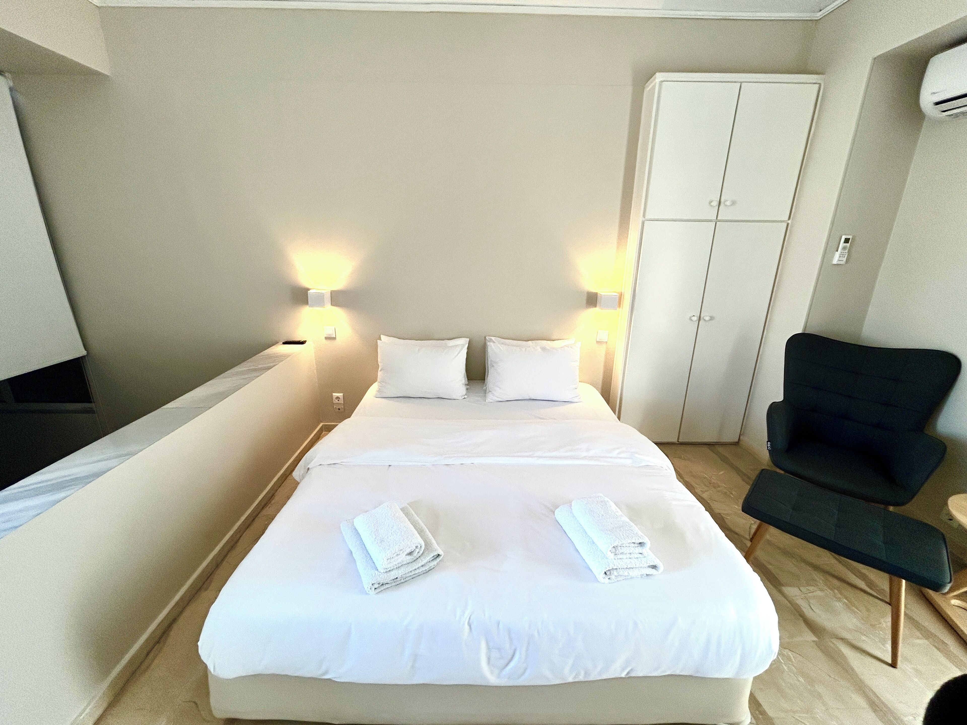 A hotel room with a bed, two bedside lamps, a wardrobe, and a chair.