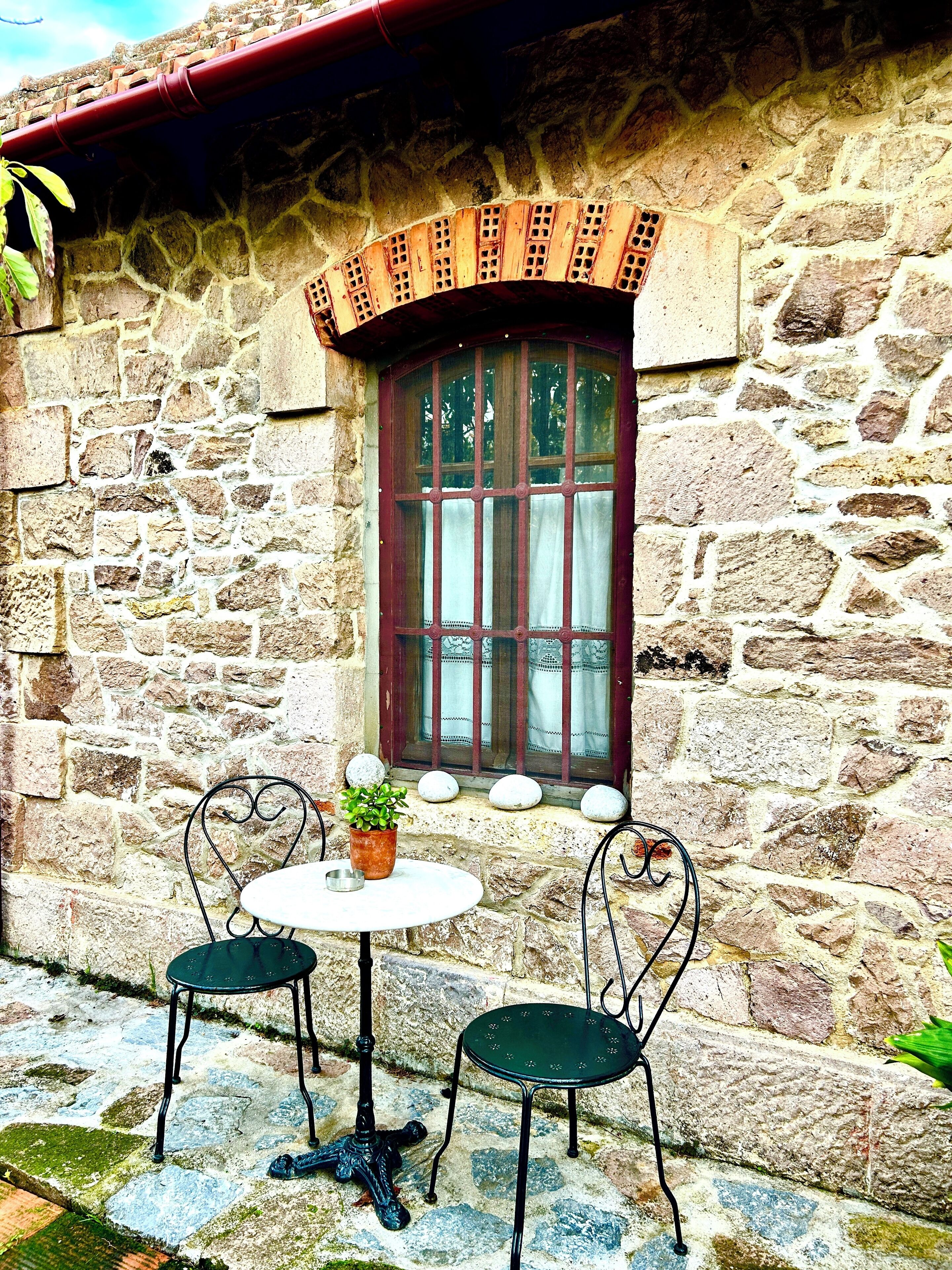 A stone building with a window, a small table with chairs, and a potted plant.