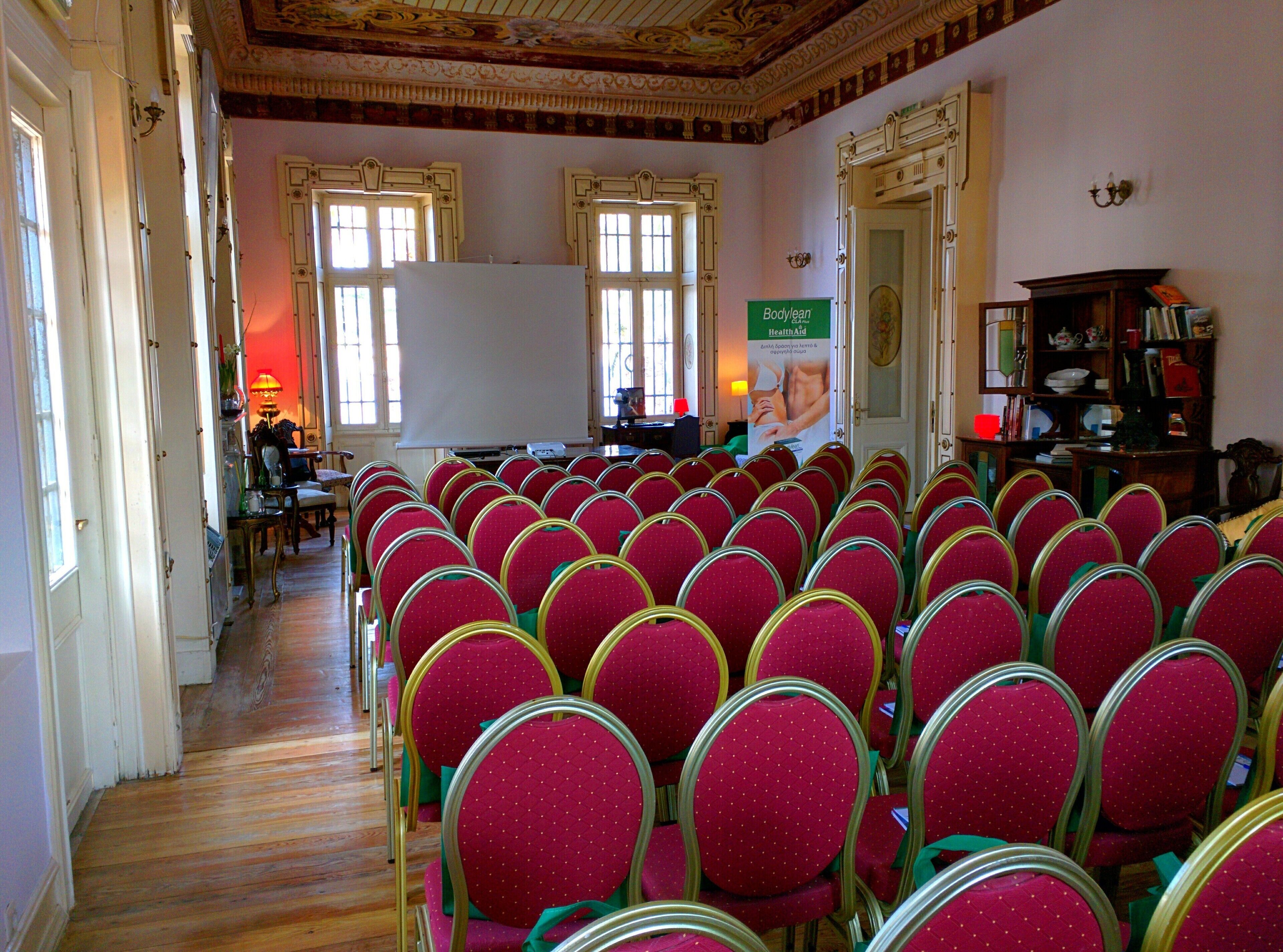 A conference room with rows of red chairs, a whiteboard, and a projector.
