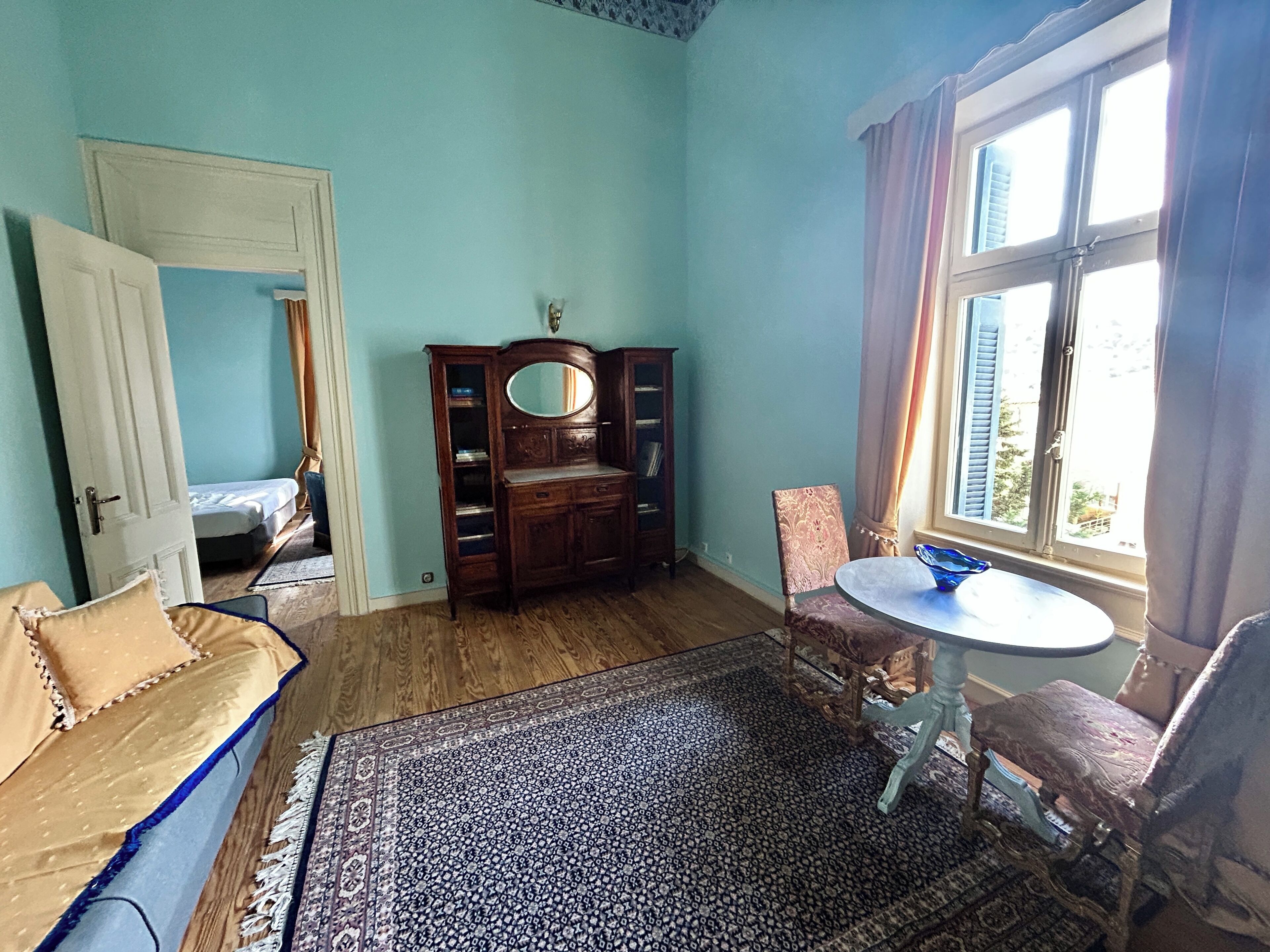 A room with a bed, a dresser, a mirror, a round table, and a window with curtains.