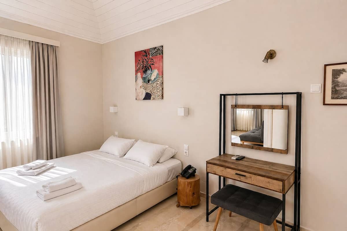 A hotel room with a bed, bedside table, chair, desk, and a painting on the wall.