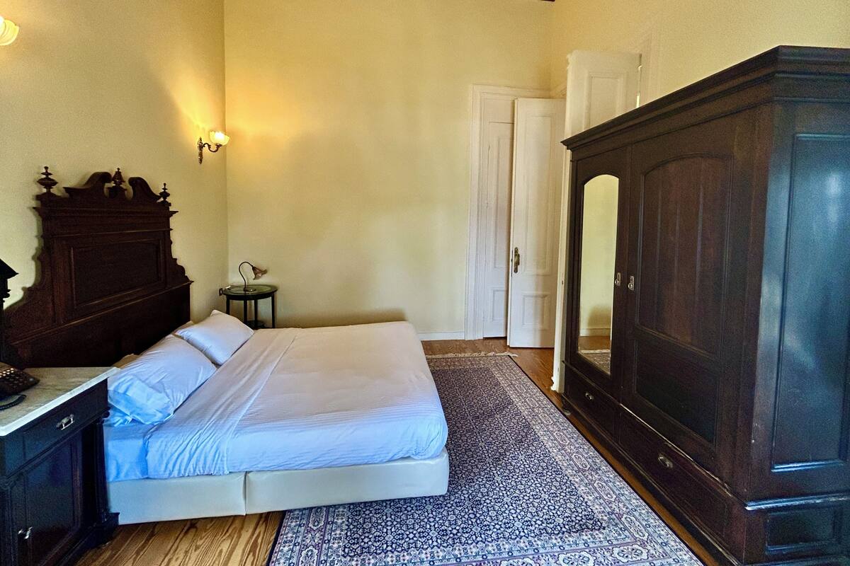 A bedroom with a bed, a dresser, a nightstand, a wardrobe, and a door.