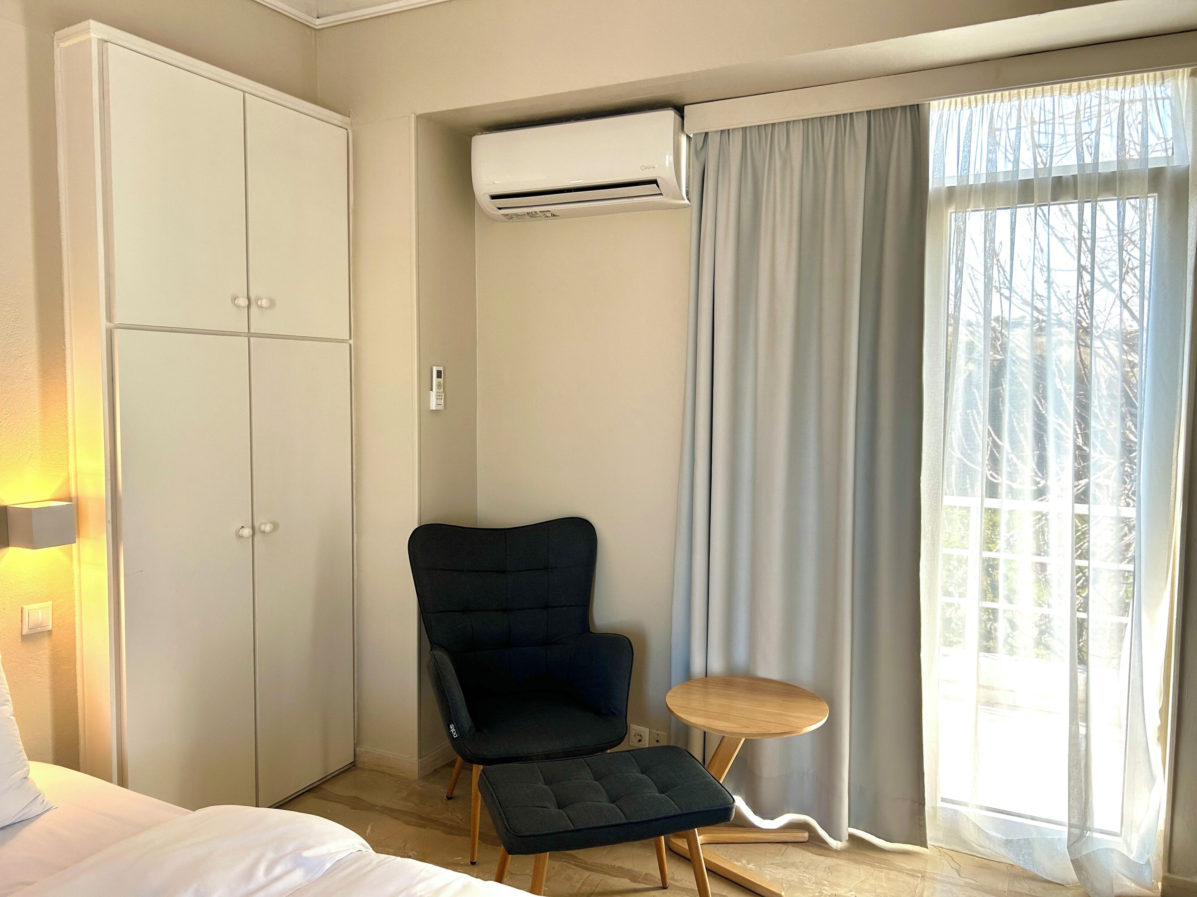 Habitació d'hotel amb llit, armari, cadira, taula petita i finestra amb cortines.
