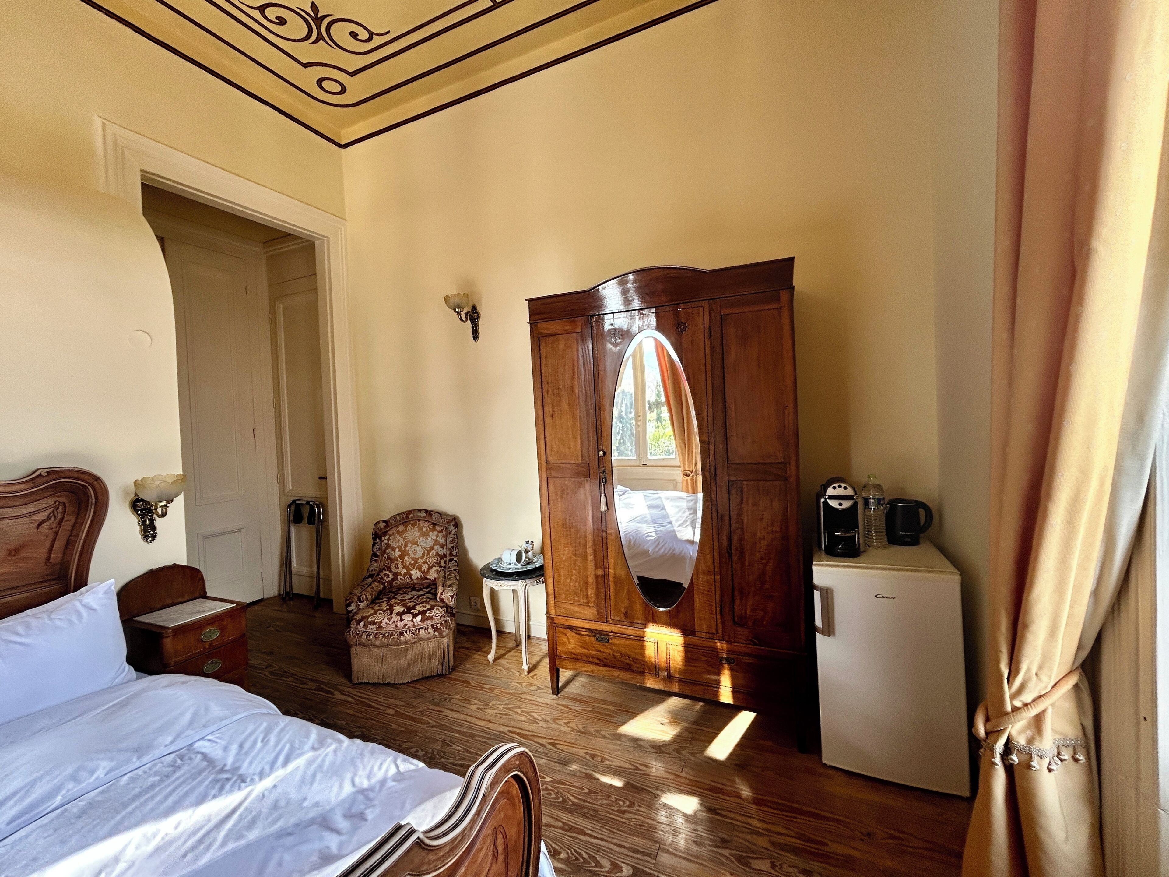 Un dormitorio con una cama de madera, una silla, una mesita, un armario y un refrigerador.