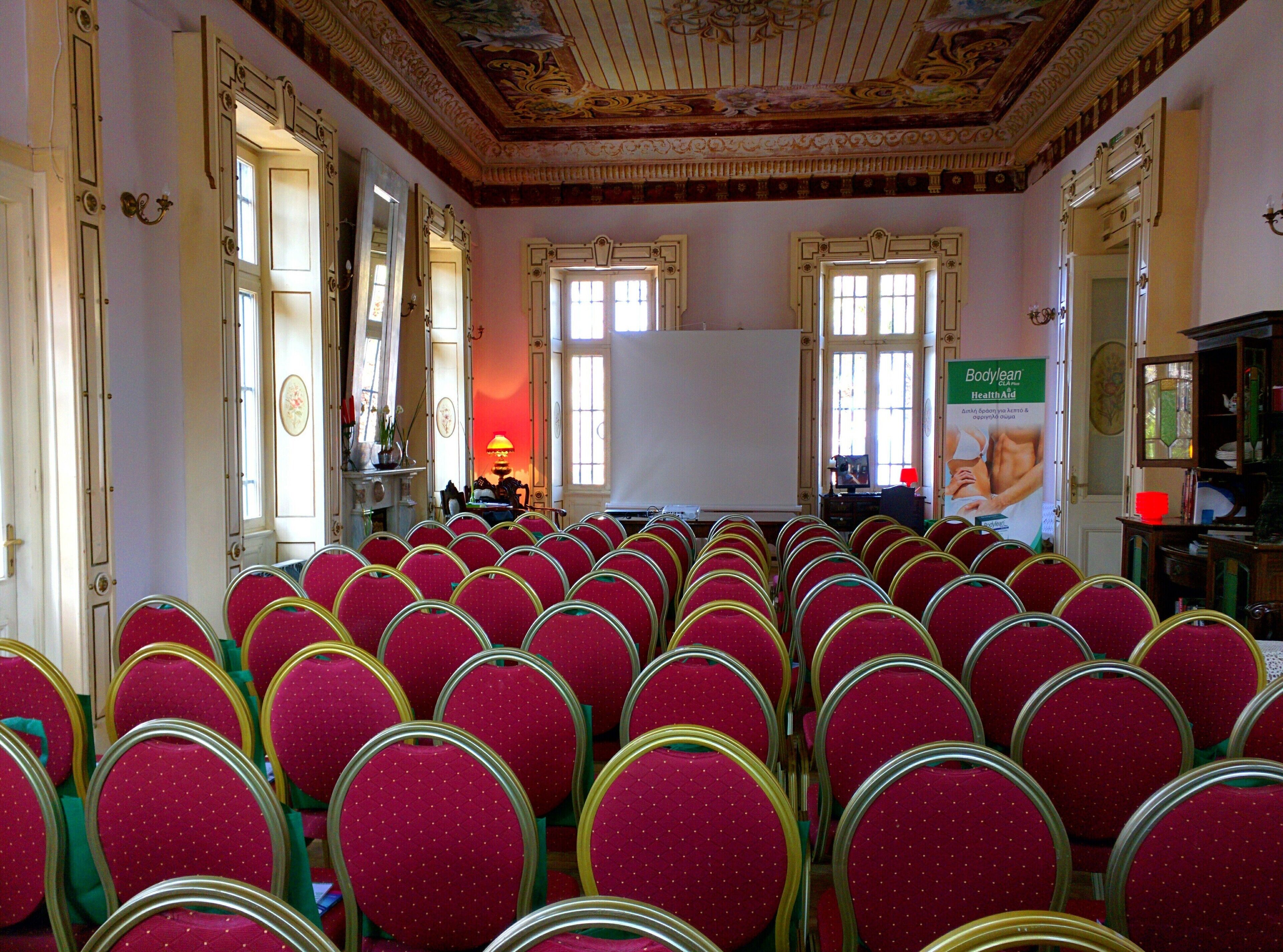 A conference room with rows of red chairs, a whiteboard, and a poster on the wall.