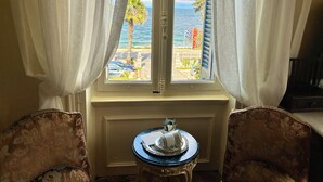 Habitación con vista al mar a través de una ventana con cortinas blancas. Hay una pequeña mesa con un adorno encima.