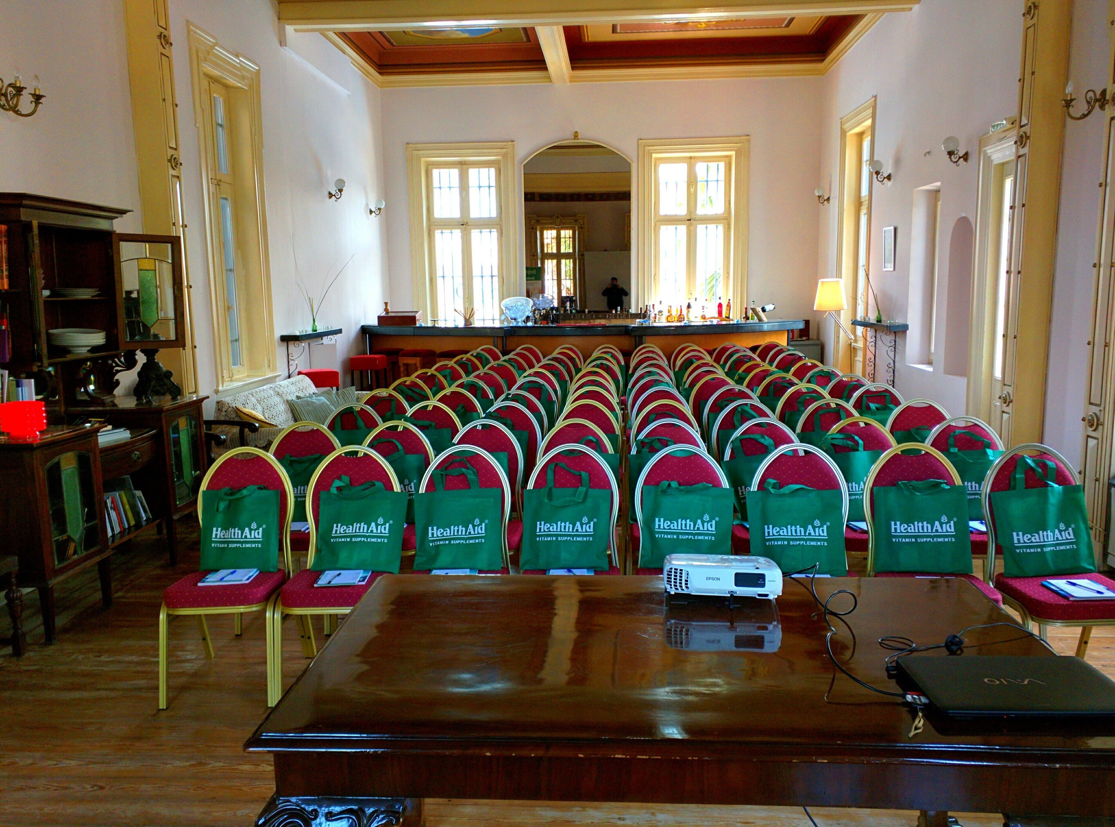 Un salón de conferencias con filas de sillas, un proyector y una mesa.