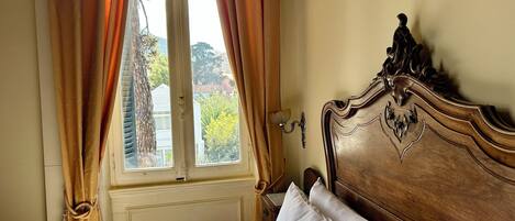 A neatly made bed with white linens, a wooden headboard with intricate carvings, and a window with curtains.