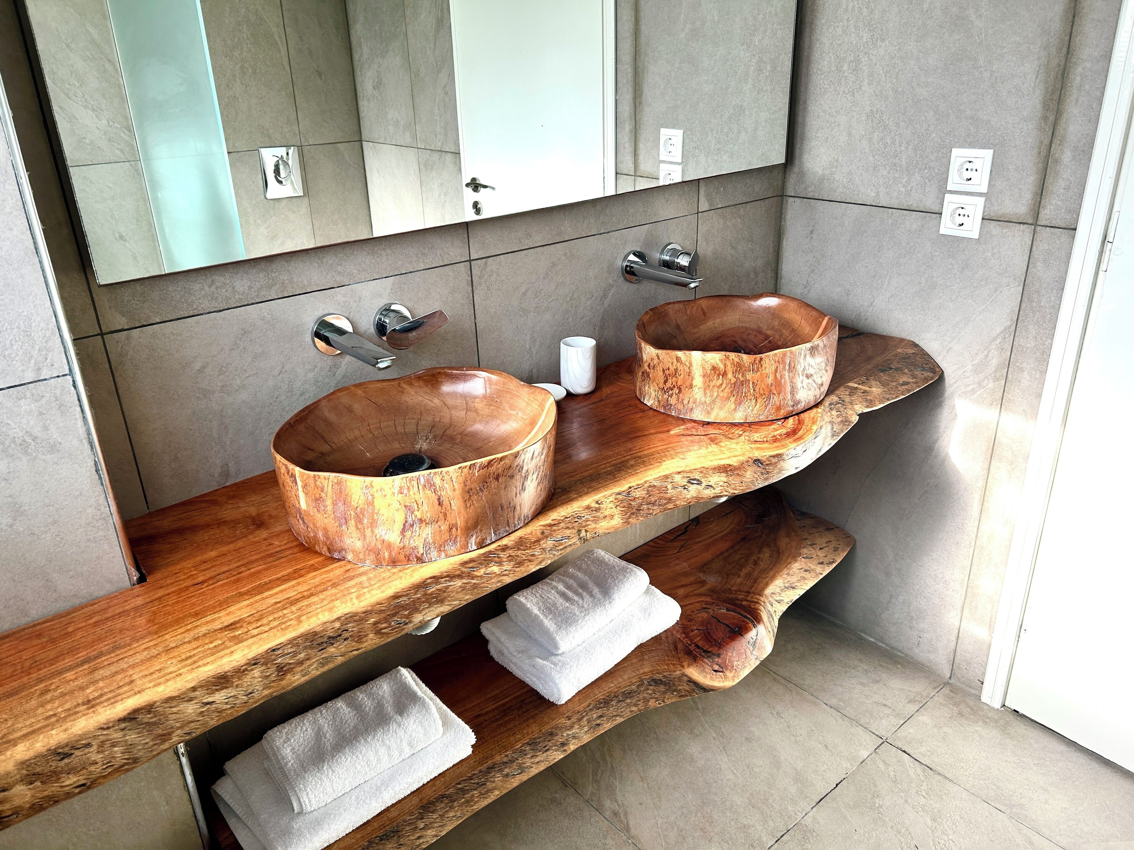Un baño con dos lavamanos de madera, un espejo y un estante de madera con toallas.
