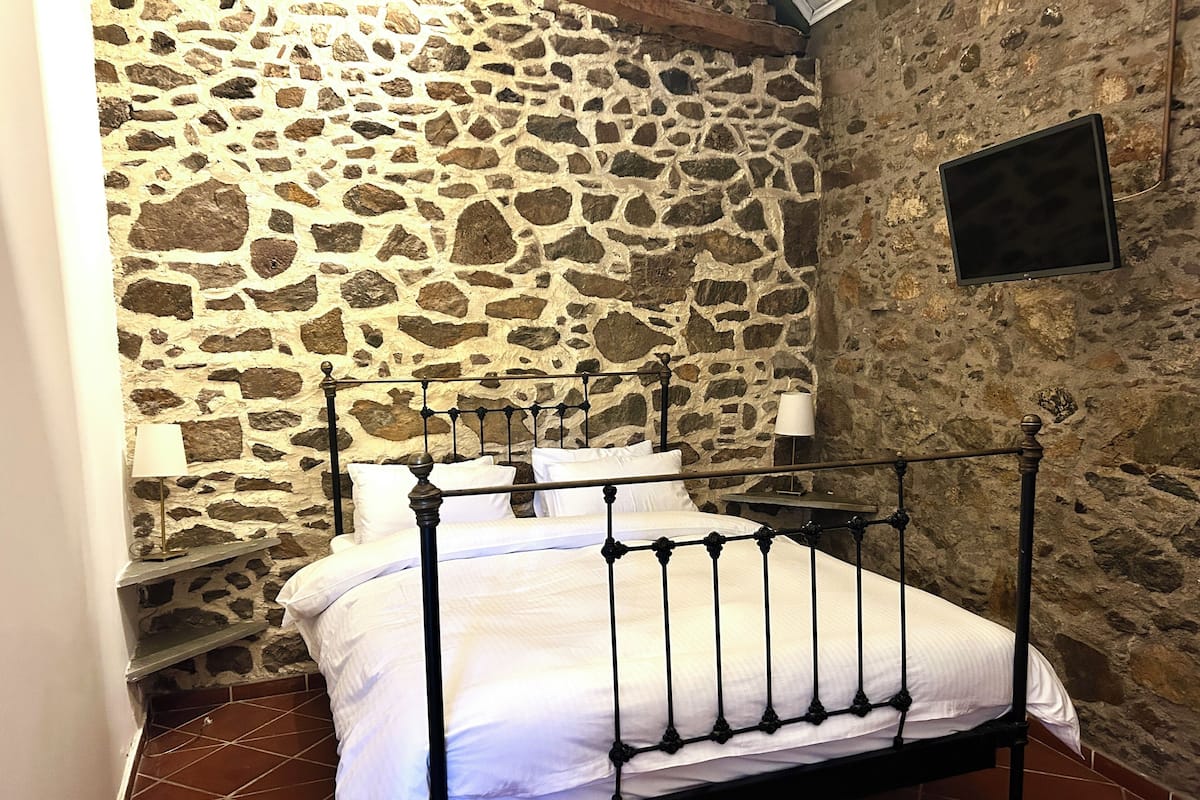 A stone-walled bedroom with a metal bed frame, white bedding, and a bedside lamp.
