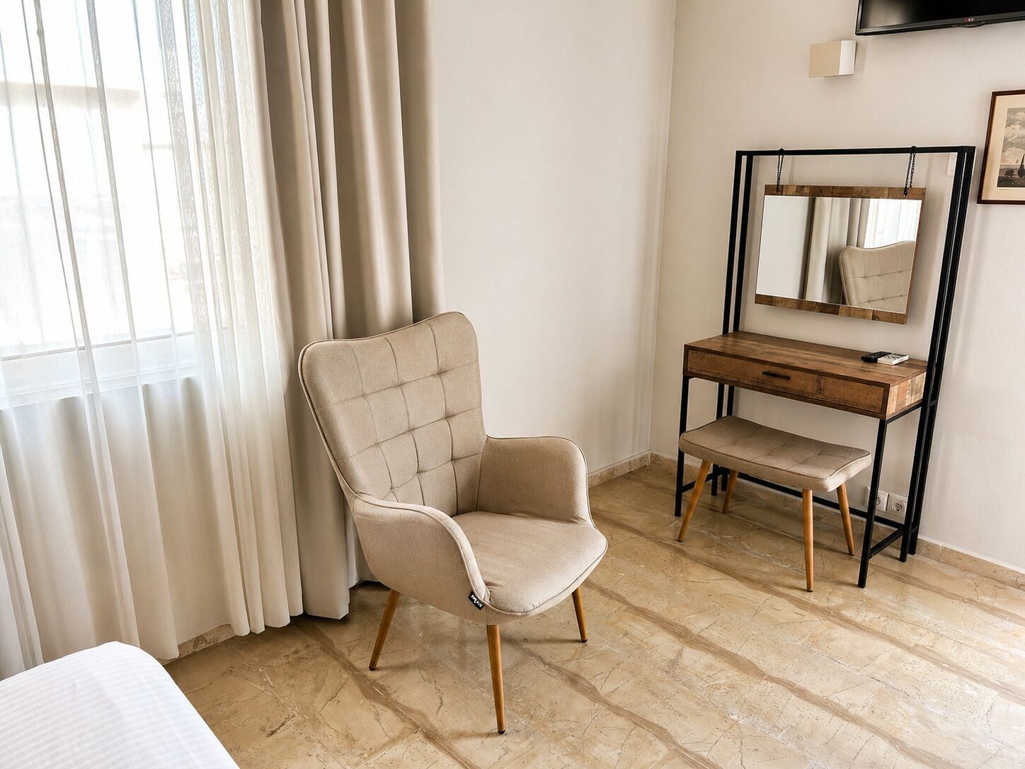 Quarto com cama, cadeira, escrivaninha, espelho e janela com cortinas.