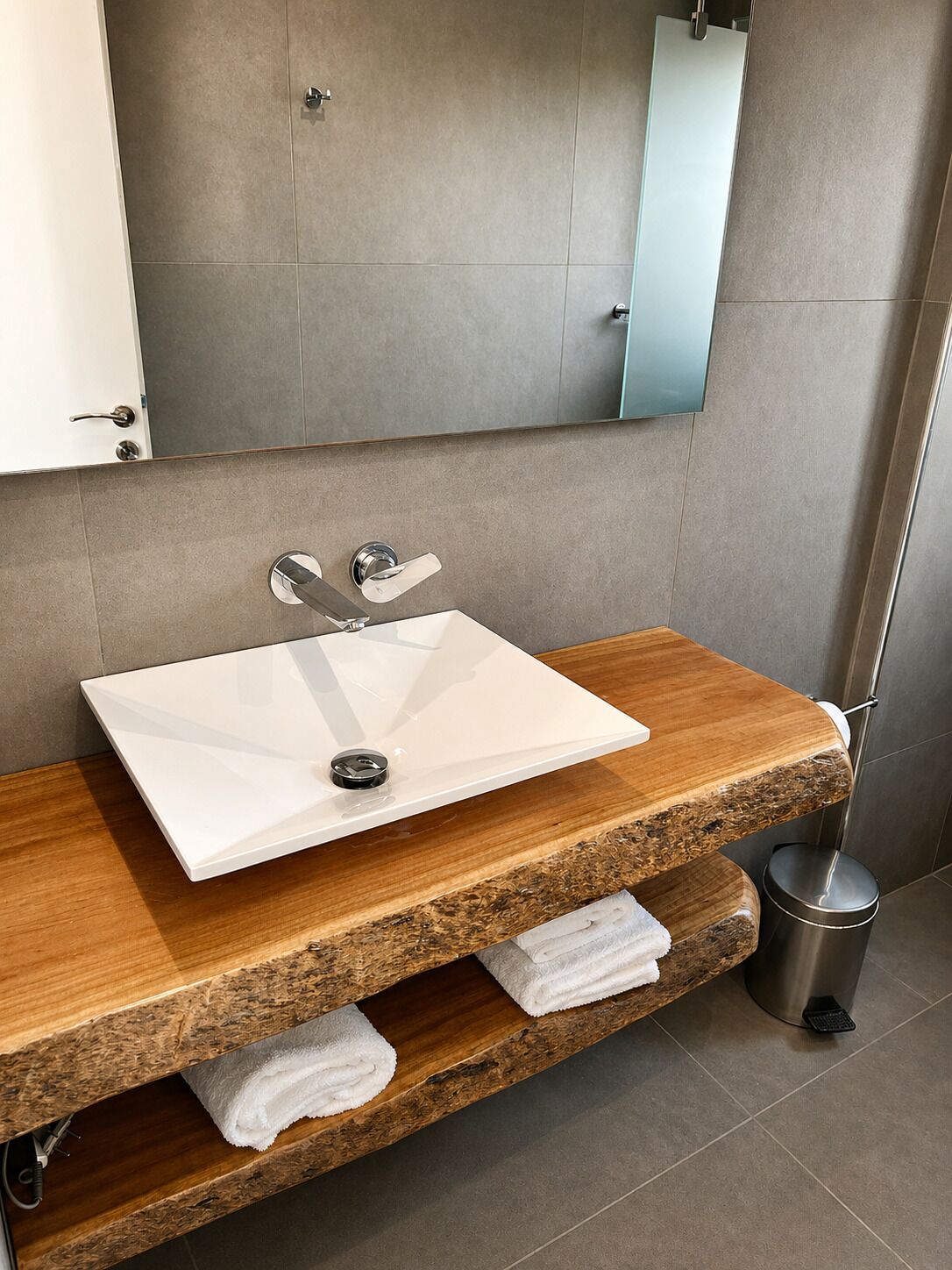 A bathroom with a white sink, wooden vanity, and a mirror.