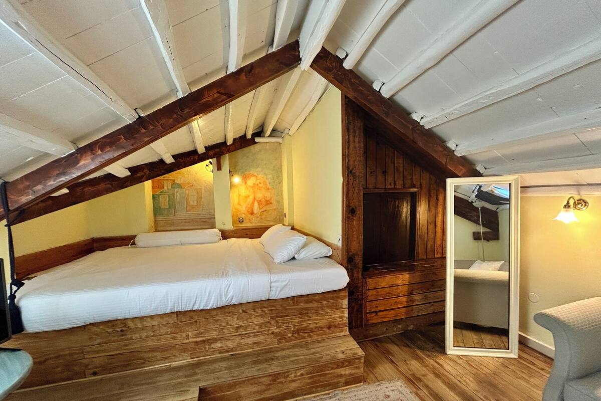 A bedroom with a wooden ceiling, a bed, a mirror, and a small table.