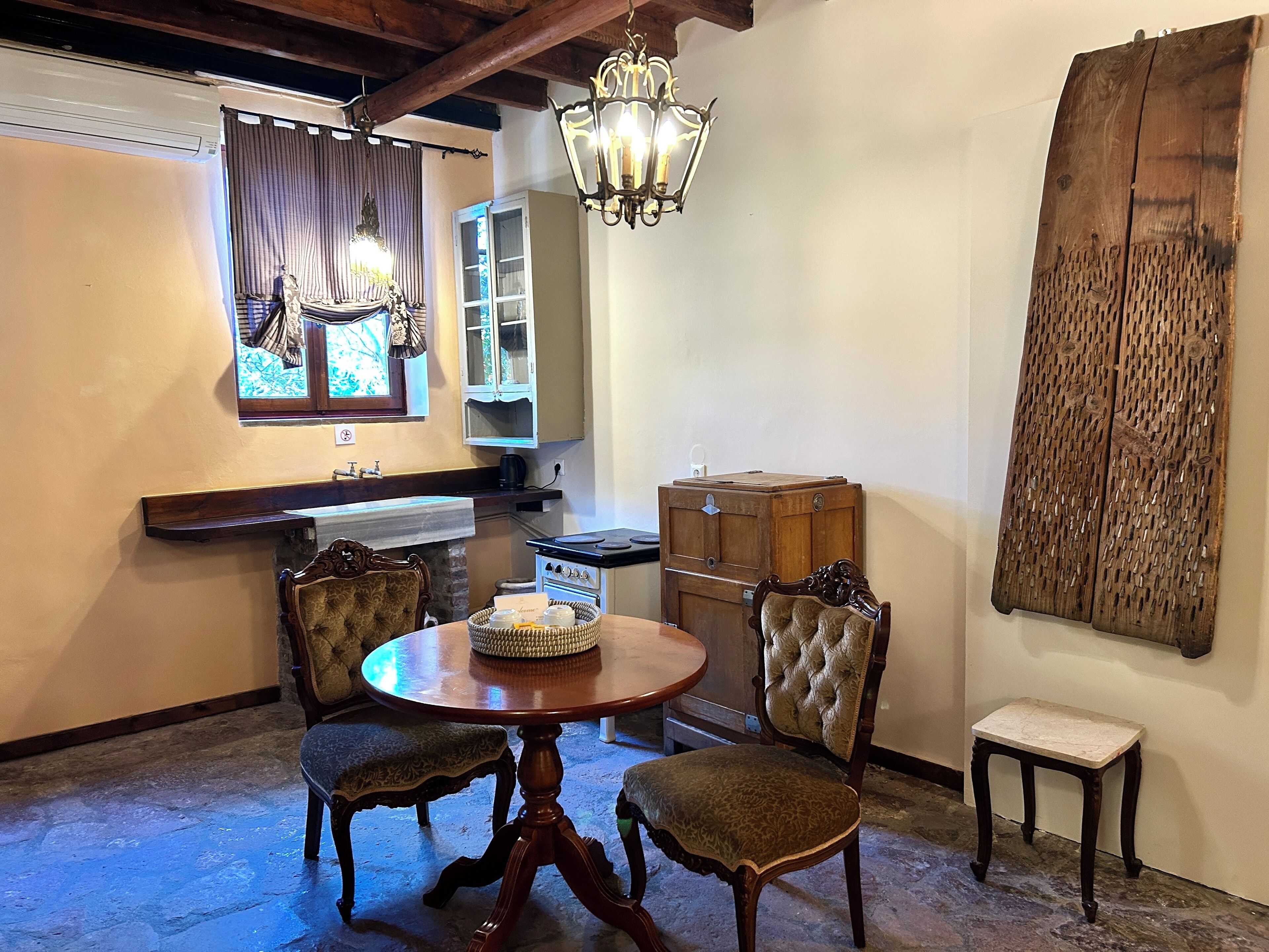A dining area with a round table, two upholstered chairs, a chandelier, a wooden cabinet, and a large wooden artwork on the wall.