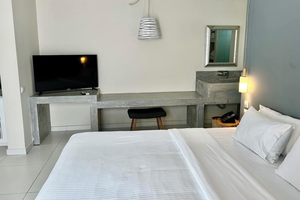 A hotel room with a bed, a desk with a TV, a mirror, and a bedside lamp.