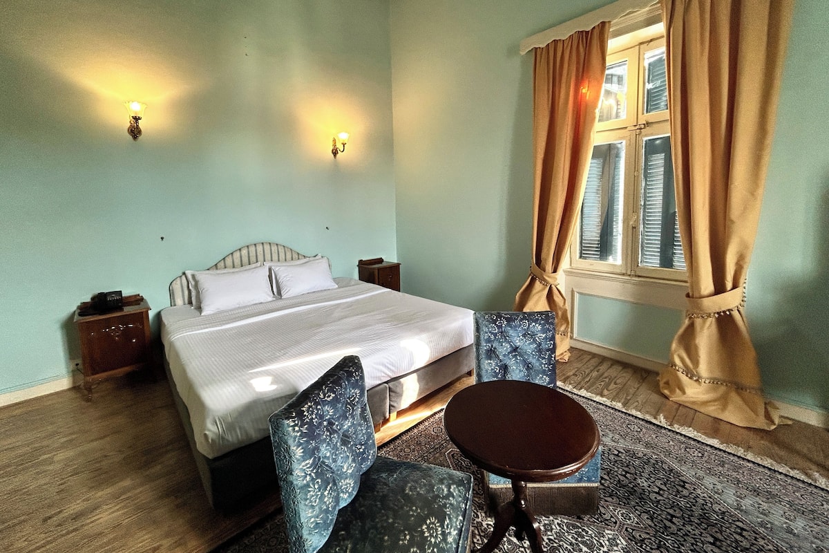 A bedroom with a bed, two nightstands, a chair, a small table, and a window with curtains.