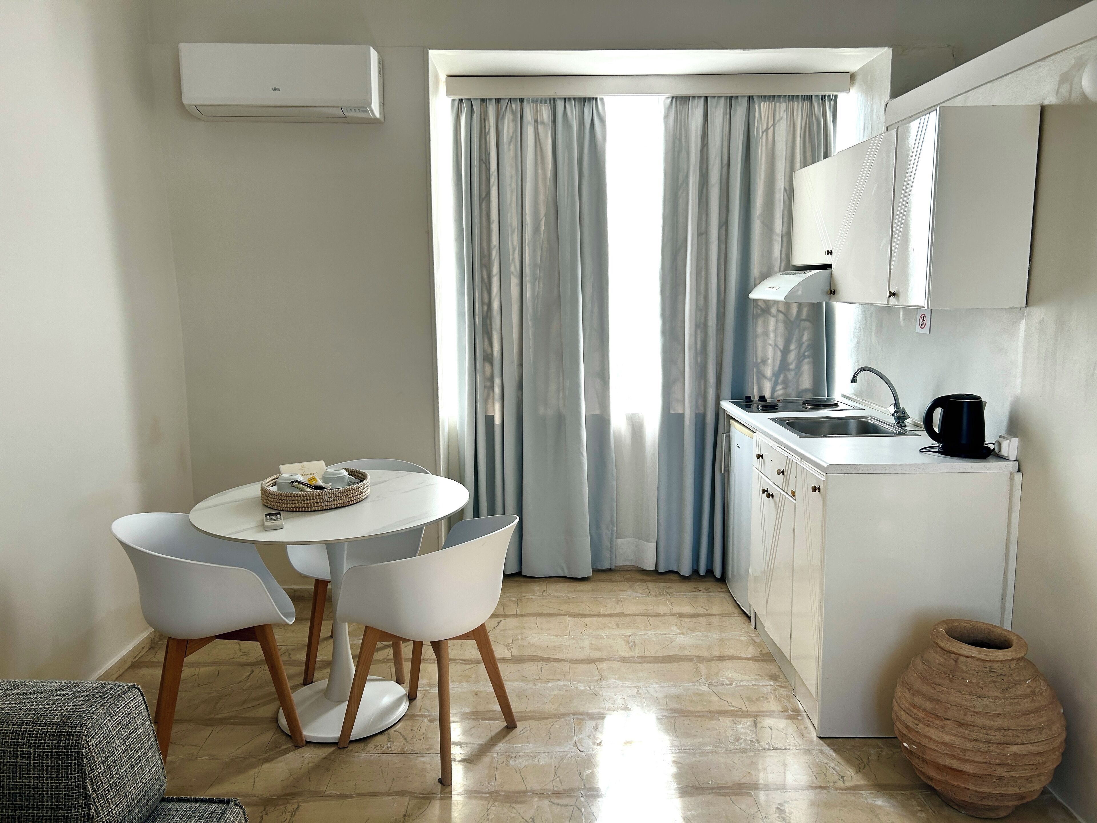 Una cocina compacta con comedor, una ventana con cortinas y una cafetera.