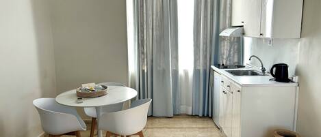 A compact kitchen with a dining area, a window with curtains, and a coffee maker.