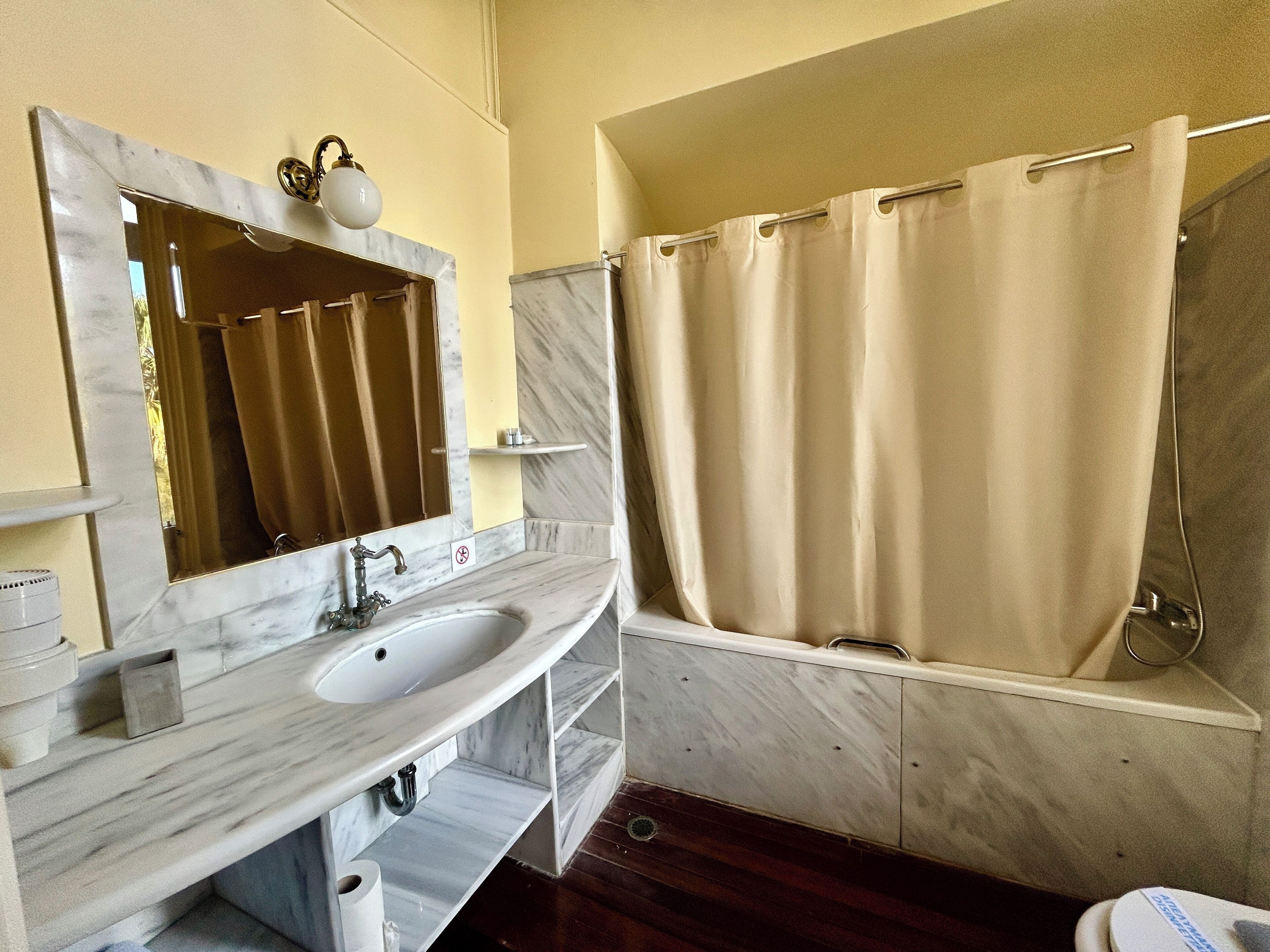 A bathroom with a marble sink, a mirror, a shower, and a towel rack.