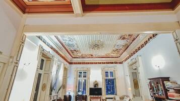 A spacious room with a high ceiling, ornate ceiling decorations, a blue sofa, and a wooden coffee table.