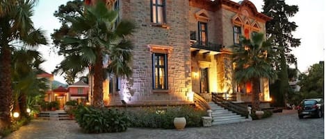 Un edificio de piedra con una escalera central, rodeado de palmeras y un camino de adoquinado.