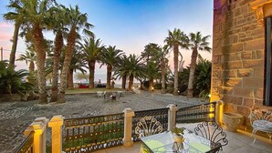 Un patio con mobiliario exterior, palmeras y vistas al mar.