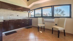 A modern kitchen with dark cabinets, a large window, and two white chairs. - ANAELEHOUSEAPARTMENTS L.T.B. (Arborea)