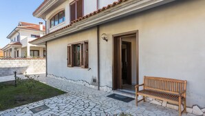 A two-story house with a tiled patio, a wooden bench, and a door leading to the interior. - ANAELEHOUSEAPARTMENTS L.T.B. (Arborea)