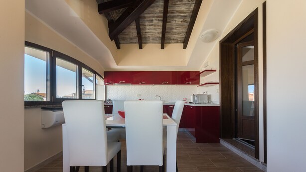 A modern kitchen with white and red cabinetry, a dining area with white chairs, and a view through large windows. - ANAELEHOUSEAPARTMENTS L.T.B. (Arborea)