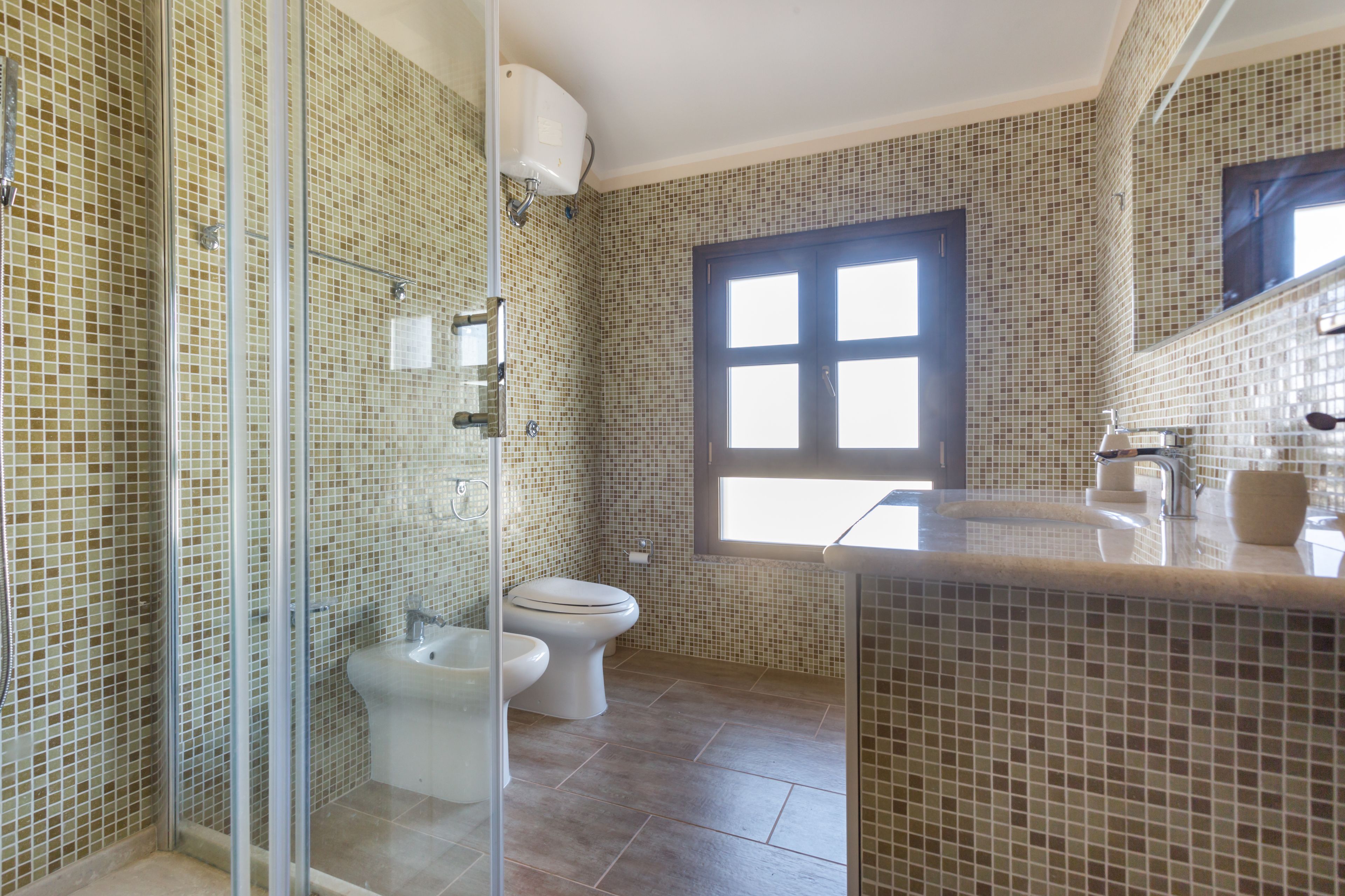 A bathroom with a glass shower enclosure, a toilet, and a sink with a mirror.
