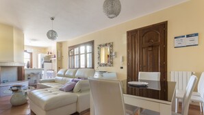 A modern living room with a white sofa, a glass coffee table, and a dining area with white chairs and a wooden table. - ANAELEHOUSEAPARTMENTS L.T.B. (Arborea)