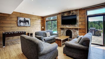 A cozy living room with a stone fireplace, comfortable seating, and a large window offering a view of the outdoors.