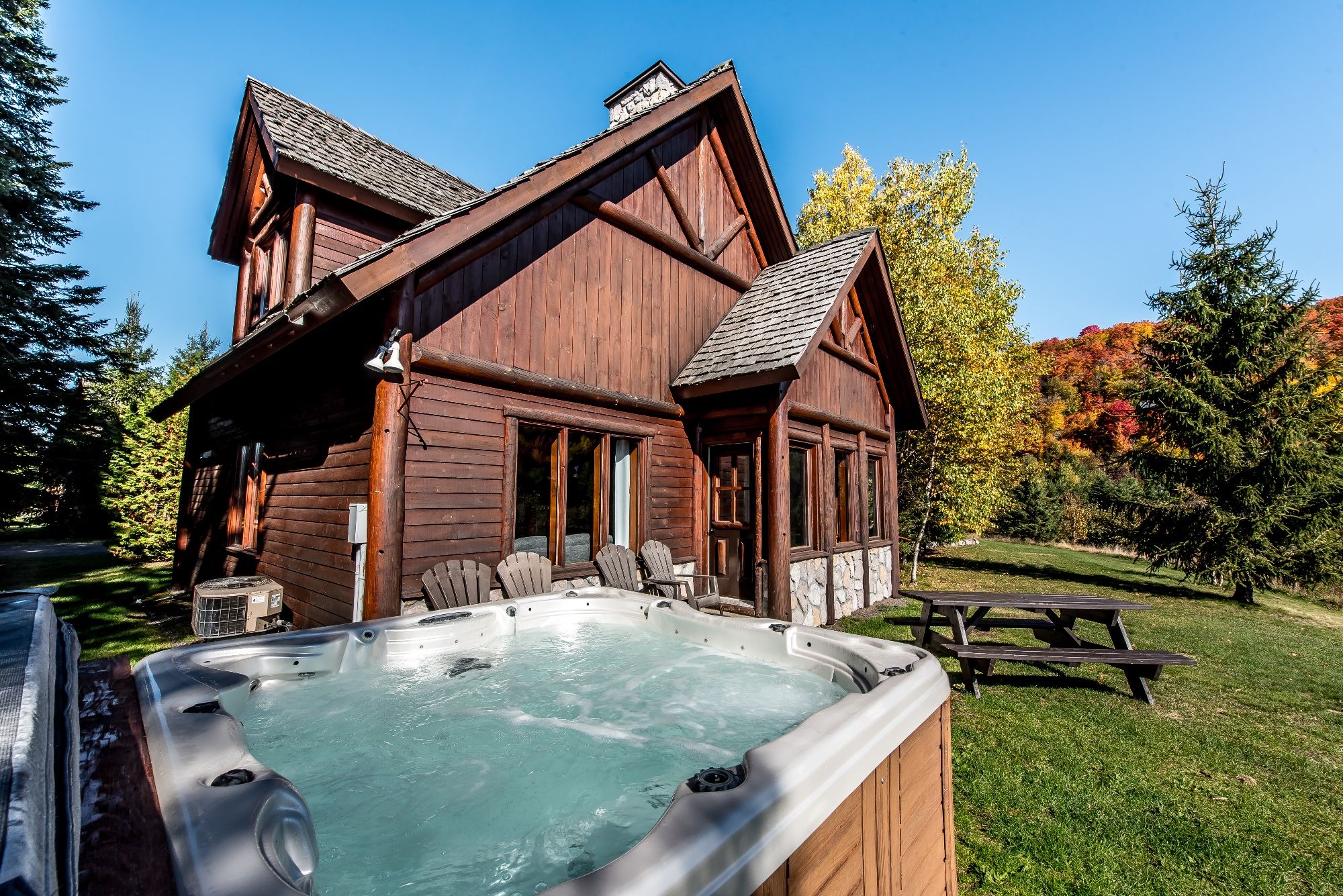 A wooden cabin with a hot tub, picnic table, and outdoor seating area.