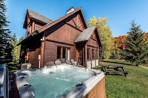 Una cabaña de madera con jacuzzi, mesa de picnic y zona de estar exterior.