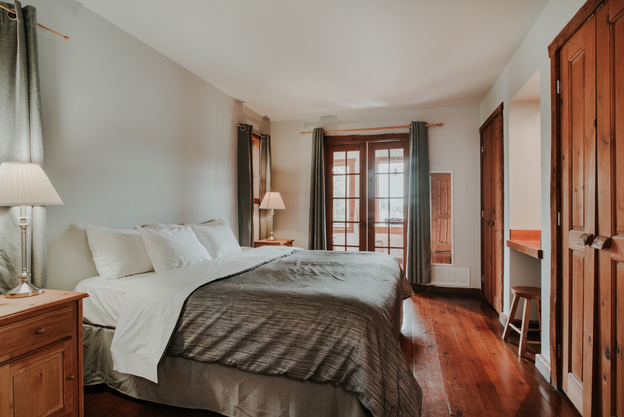 Un dormitorio con cama, mesitas de noche, lámpara y vistas por la ventana.