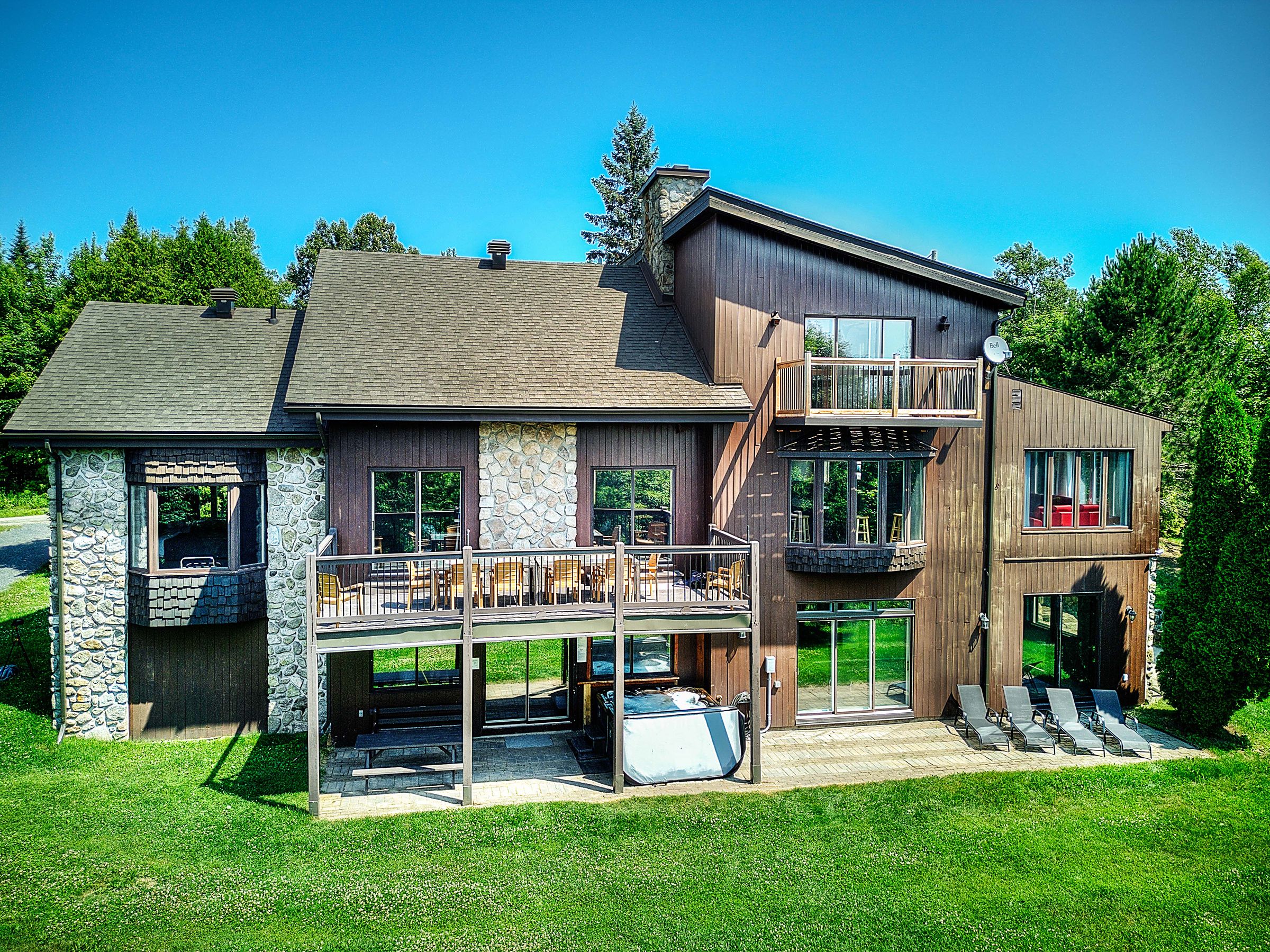 Ein zweigeschossiges Haus mit einer Steinfassade, einem Balkon und einer überdachten Terrasse.