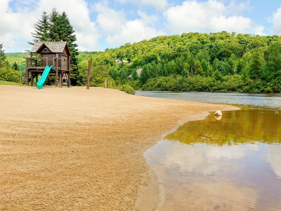 Ein Sandstrand mit einer Holzspielanlage und einem kleinen Haus im Hintergrund.
