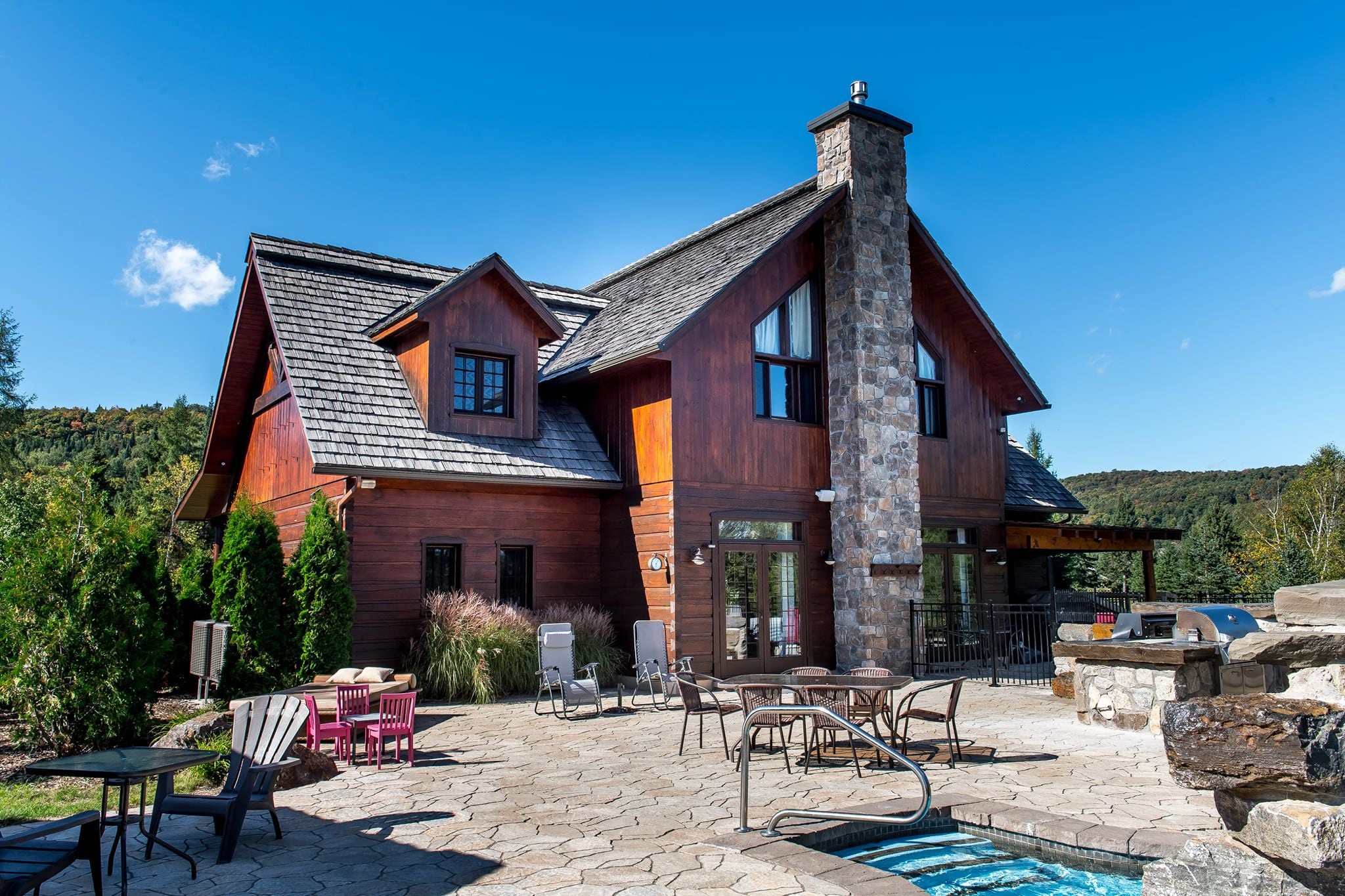 A large wooden house with a stone chimney, outdoor seating, and a swimming pool.